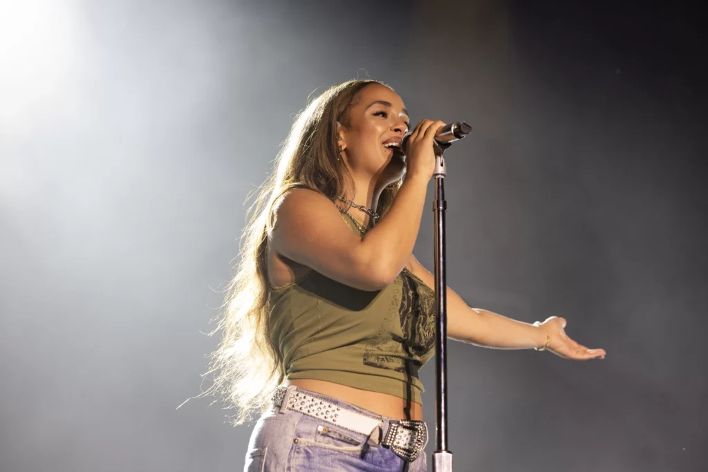 Jorja Smith performing live on stage, singing passionately with stage lights in the background during her 2025 tour.