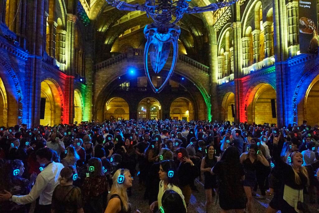 Silent Disco party in London at the Natural History Museum with people dancing to three DJs. Let me know if you need any further tweaks! People dancing at the Silent Disco party in London at the Natural History Museum, wearing wireless headphones