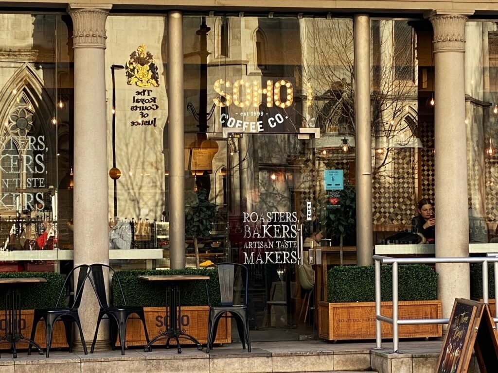 Soho Coffee – A Cozy Café with a Legal Landmark View Soho Coffee shop near the Royal Courts of Justice, featuring outdoor seating with a view of the grand Gothic architecture