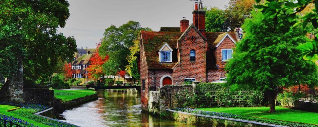 A historic view of Canterbury in Kent, featuring the grand Canterbury Cathedral, charming medieval streets, and visitors enjoying a boat ride on the River Stour