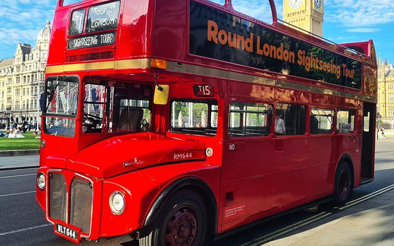 Hop-On Vintage Bus Tour Famous Places to Visit in London HouseToMotive A classic red vintage bus driving through the streets of London, offering a scenic tour of the city