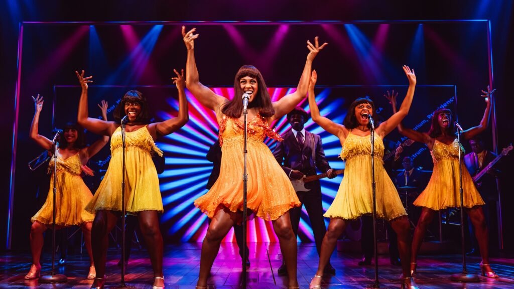 Karis Anderson performing as Tina Turner in Tina Turner Musical London, with an energetic cast behind her – HouseToMotive Karis Anderson as Tina Turner in Tina Turner Musical London, delivering a powerful live performance with the supporting cast behind her on stage